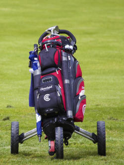 Photo of a golf bag, and clubs on a push golf cart.